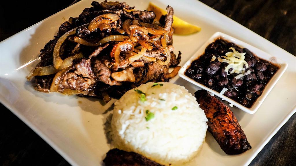 Bistec Encebollado · Marinated steak sauteed with grilled onions. Served with sweet plantains, white rice and black beans.