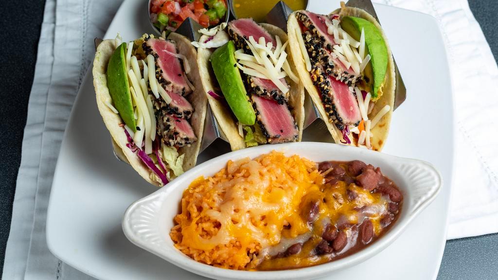 Seared Ahi Tuna Tacos · Three corn tortillas, lettuce, Monterey jack cheese, avocado, and ginger-soy dressing. Served with rice and beans.