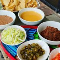 Assembly Nachos · Assemble you own nachos. Bulk order of chips, queso, beans, lettuce, tomatoes, jalapeños and...