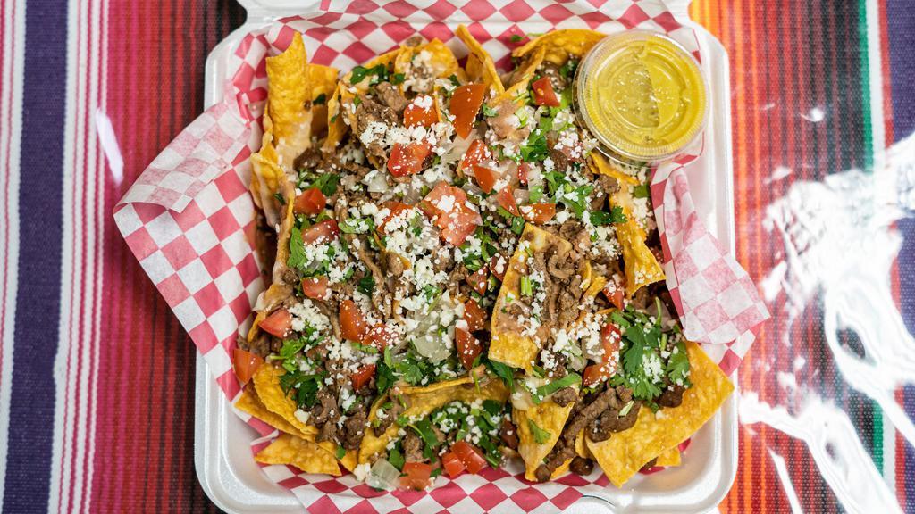 Nachos · Chips covered in beans, white melted cheese, any meat of your choice, cilantro, onions, tomatoes, and cotija cheese