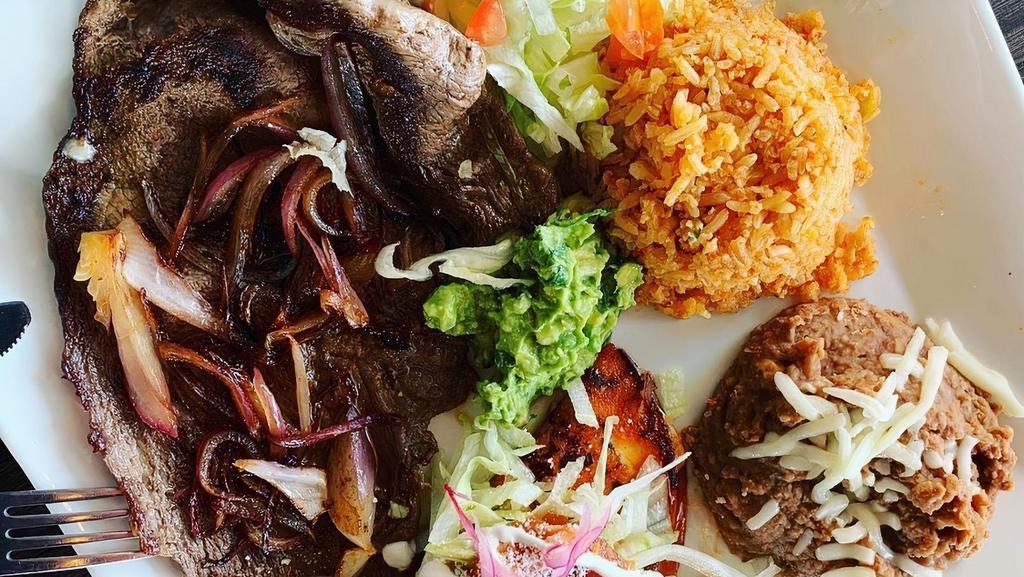 Bistec Tampiquena · Steak cooked with sauteed onions and served with a red sauce enchilada with lettuce, fresh guacamole rice and beans and a side of tortillas.
