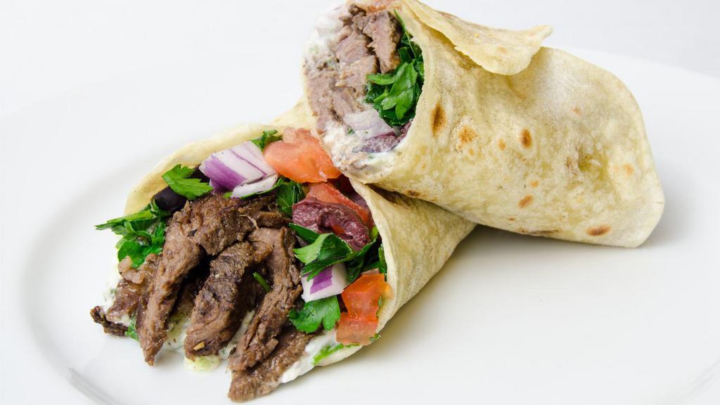 Beef Shawarma Wrap · A flour tortilla with skirt beef steak, red onions, parsley, sumac mix, diced tomatoes, pickled cucumbers, tahini sauce, and hummus spread.