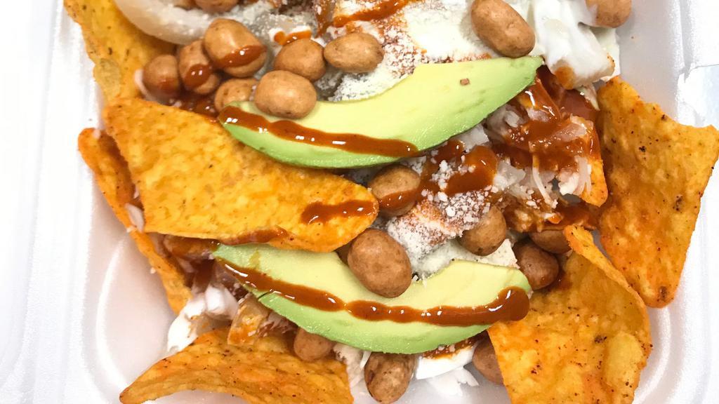 Dorilokos · Doritos topped with, cabbage, pork rinds, japanese style peanuts, avocado, sour cream, cheese and hot sauce.