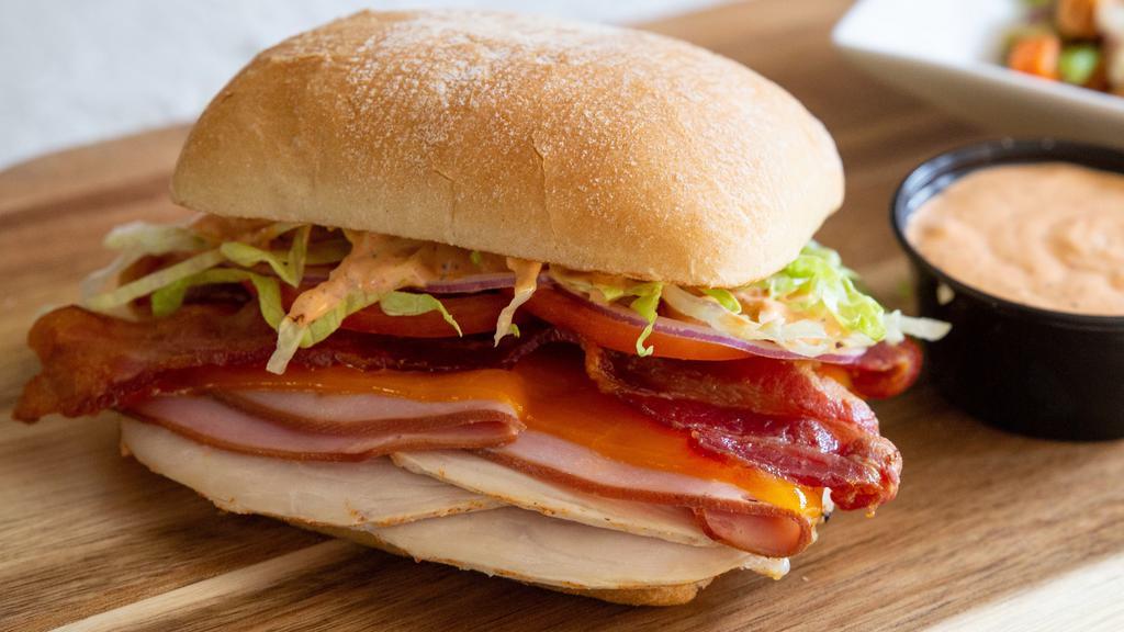 Nashotah Sunset Sandwich · Red pepper pesto spread on a toasted ciabatta with our rotisserie turkey, ham, bacon, cheddar, lettuce, tomato and onion.