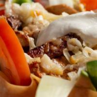 Grilled Steak Taco Salad · Crisp flour shell filled with refried beans, lettuce, and grilled steak. Topped with shredde...