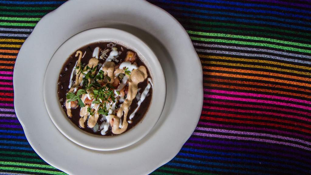 Black Bean Soup · Hearty black beans, simmered with fresh epazote, topped with spicy chipotle sauce, sour cream, onions, cilantro and tomato.