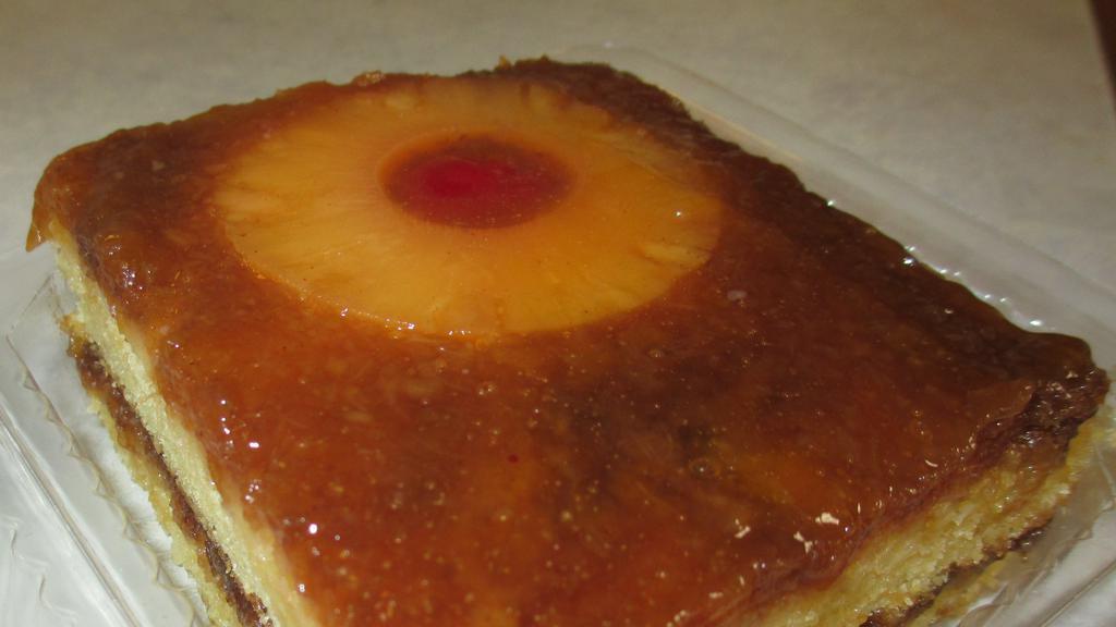 Pineapple Upside Down Cake Slice · Our moist yellow cake baked with Pineapple rings and brown sugar and Maraschino Cherries!