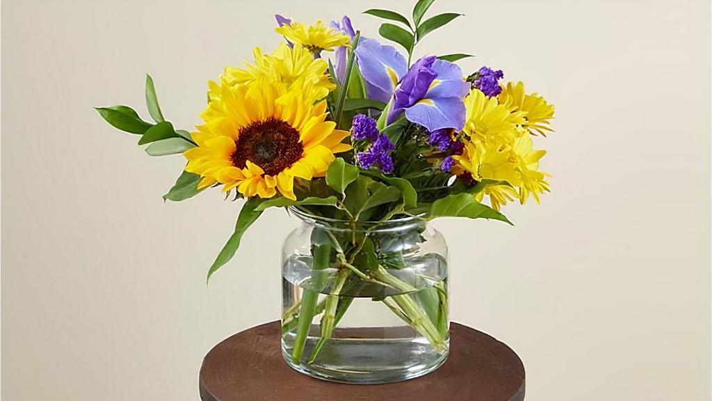 Flutter By · The cheerful Flutter By Bouquet is guaranteed to make every recipient smile. Designed with energetic yellow sunflowers and daises that are beautifully contrasted by blue iris. This arrangement is the perfect addition to a surprise birthday party or just a 'thinking of you' gift. Vase included. Please Note: The bouquet pictured reflects our original design for this product. While we always try to follow the color palette, we may replace stems to deliver the freshest bouquet possible. Item # M2S
