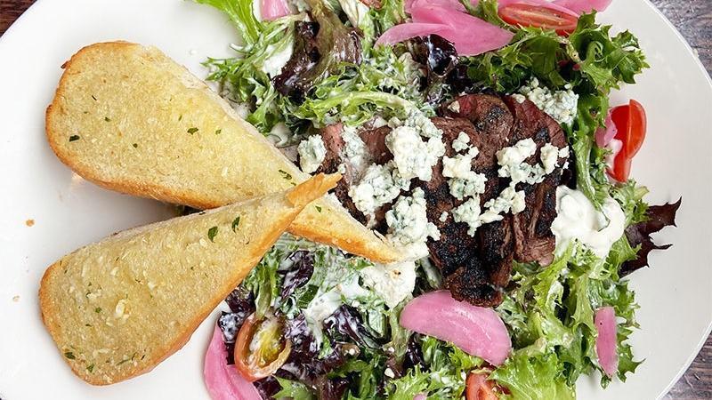 Top Sirloin Salad · grilled top sirloin on a bed of arcadian greens tossed in bleu cheese dressing with grape tomato, pickled red onion and bleu cheese crumbles. served with buttered garlic toast.