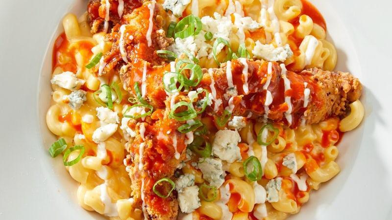 Buffalo Mac & Cheese · macaroni and cheese tossed with buffalo sauce, topped with buttermilk-fried chicken strips and finished with creamy ranch dressing, bleu cheese crumbles, and green onions.