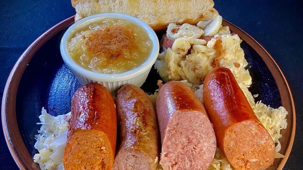 Old World Sausage Sampler · A combination of four sausages from famous recipes of the J. Fred Schmidt Packing Company established in 1886. Served over hot kraut und pork with our German Potato Salad, Chunky Applesauce, und split top bun.