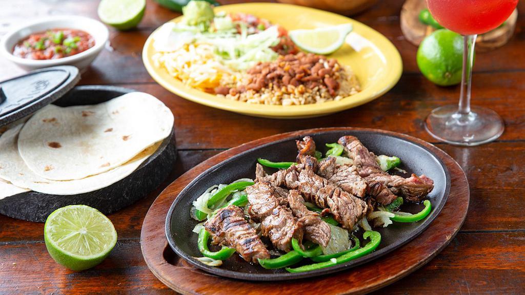 Steak Fajitas* · Tender, marinated steak served on a sizzling skillet with freshly grilled onions and peppers. Served with fresh tortillas, charro beans and rice, lettuce, cheese, pico de gallo, sour cream and guacamole.