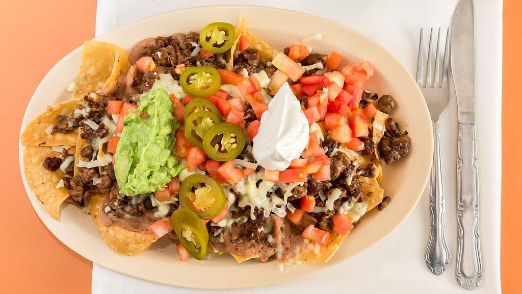 Nacho Supremos · A mound of tortilla chips topped with ground beef and chihuahua cheese beans, tomato, jalapeno slices served with guacamole and sour cream.