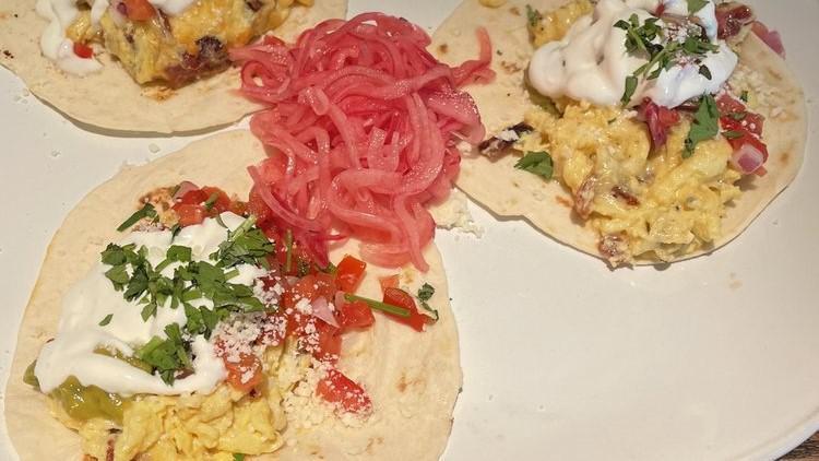 Breakfast Tacos · Three corn or flour tortillas filled with scrambled eggs, guacamole, cotija cheese, crème fraîche, green chile hollandaise, pico, cilantro • Add extra taco +2.5