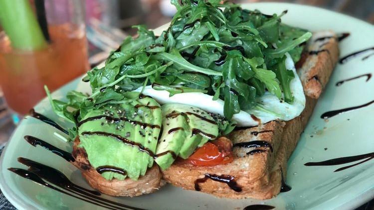 Avocado Toast · Whole wheat toast, sliced whole avocado, roasted campari tomatoes, two eggs your way, topped with arugula salad tossed with champagne vinaigrette and a balsamic glaze drizzle