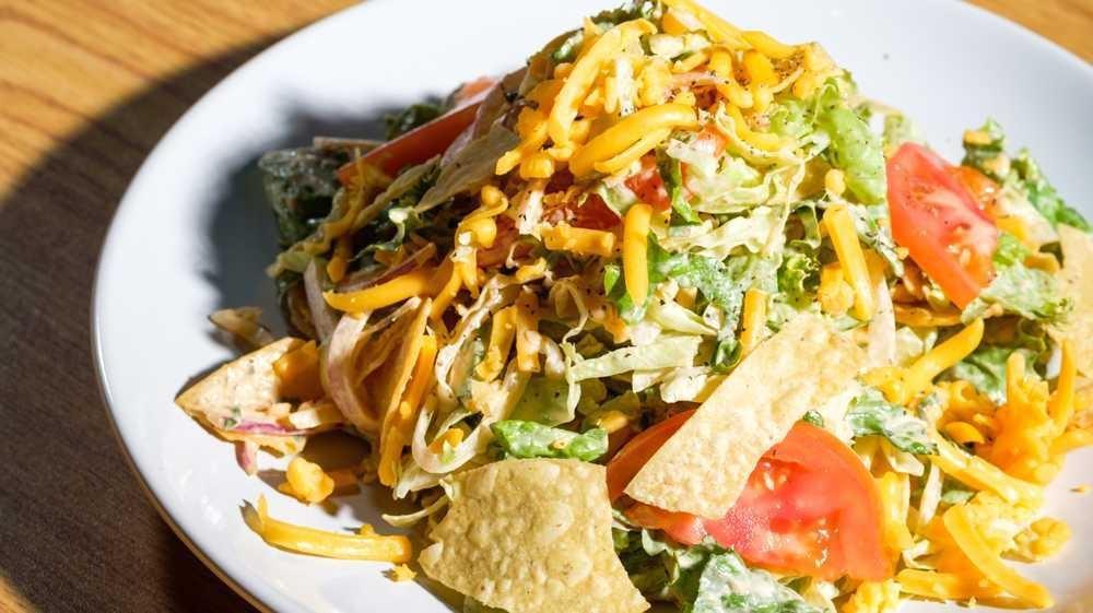 Smashed Taco Salad · Chopped buttercrunch lettuce, vine-ripe tomato, shaved red onion, cheddar cheese, tortilla chips, black pepper, chipotle buttermilk dressing.