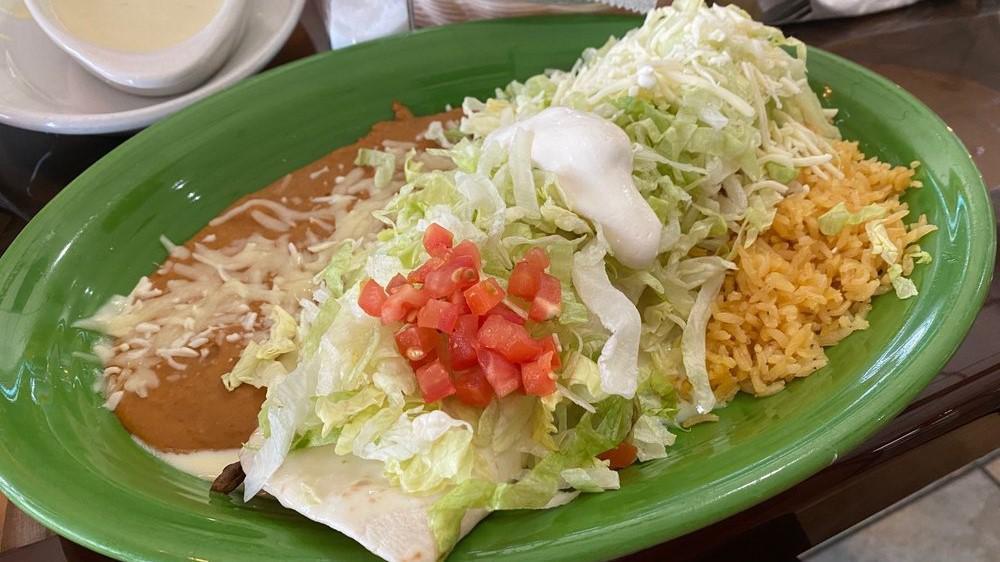 Fajita Burrito · Your choice of grilled chicken or steak, grilled onions, bell peppers and tomatoes, smothered in queso sauce and red sauce. Topped with lettuce, tomato, sour cream. Served with rice and beans.