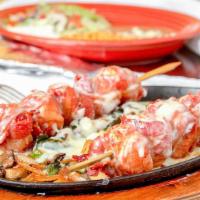 #58. Camarones Rellenos · Bacon wrapped shrimp with ham in A hot skillet. Covered with melted cheese on A bed of onion...