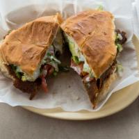 Torta De Milanesa De Res / Breaded Beef Torta · Con frijoles, crema, lechuga, tomate y aguacate. / Served with beans, sour cream, lettuce, t...