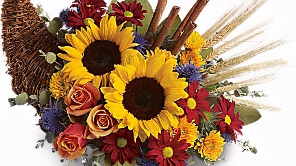 Classic Cornucopia · Along with joy, this cornucopia carries an abundance of beautiful fall flowers and foliage. A stunning centerpiece or inviting entryway display, this beauty will be at home anywhere in the house.
Dazzling sunflowers, light orange roses and spray roses, red daisy spray chrysanthemums, yellow cushion spray chrysanthemums, eucalyptus, magnolia leaves, cinnamon sticks and wheat are perfectly arranged in a wicker cornucopia. Now you know why cornucopia translates to 