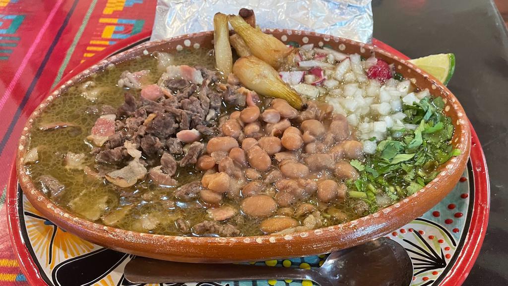 Carne En Su Jugo · Carne Asada in it’s juices Stew

Bistec & bacon pan cooked until it releases it juices, then simmered in a garlic, cilantro & onion flavored water. It’s then topped with whole beans, grilled onions. Served with a side of cilantro, diced onions, diced turnip & tortillas