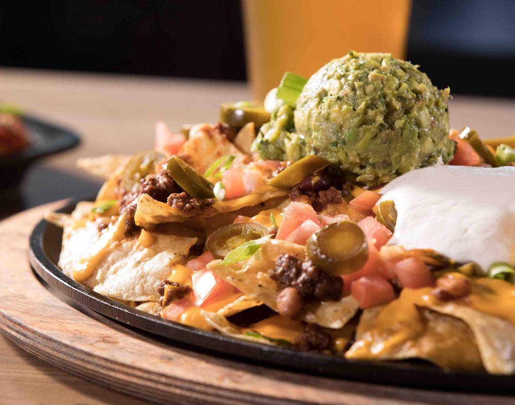 Loaded Nachos · Tortilla chips, chef-made chili, cheddar cheese sauce, jalapeños, tomatoes, sour cream, green onions.