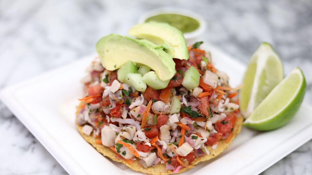 Fish Tostada · Fish ceviche on a corn tostada with slices of avocado.
