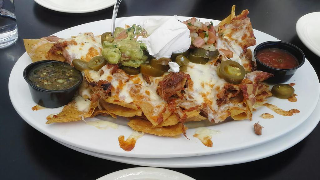 Nachos Grande · A heaping pile of chips with chihuahua cheese, refried beans, guacamole, jalapeno slices, sour cream, and pico de gallo.