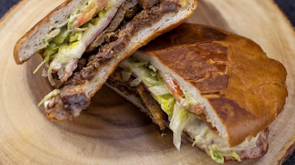Torta Cubana · Filled with skirt steak, breaded steak, ham, beans, cheese, lettuce, tomatoes, guacamole, and sour cream.