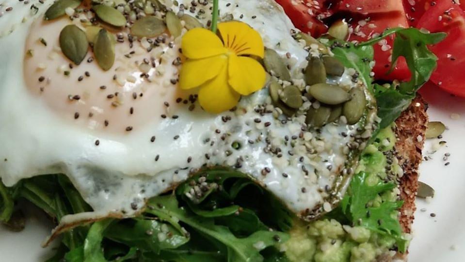 Seeded Avocado Toast · Seeded whole grain toast, seasoned smashed avocado, Campari tomatoes, arugula salad and crowned with an egg. Finished with a balsamic reduction and more seeds. Served with one side.