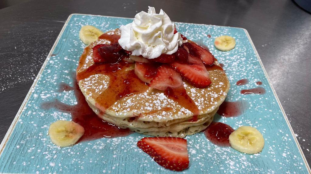 Strawberry Banana Pancakes · Four pancakes filled with fresh slices of banana and topped with fresh bananas, strawberry compote and whipped cream.