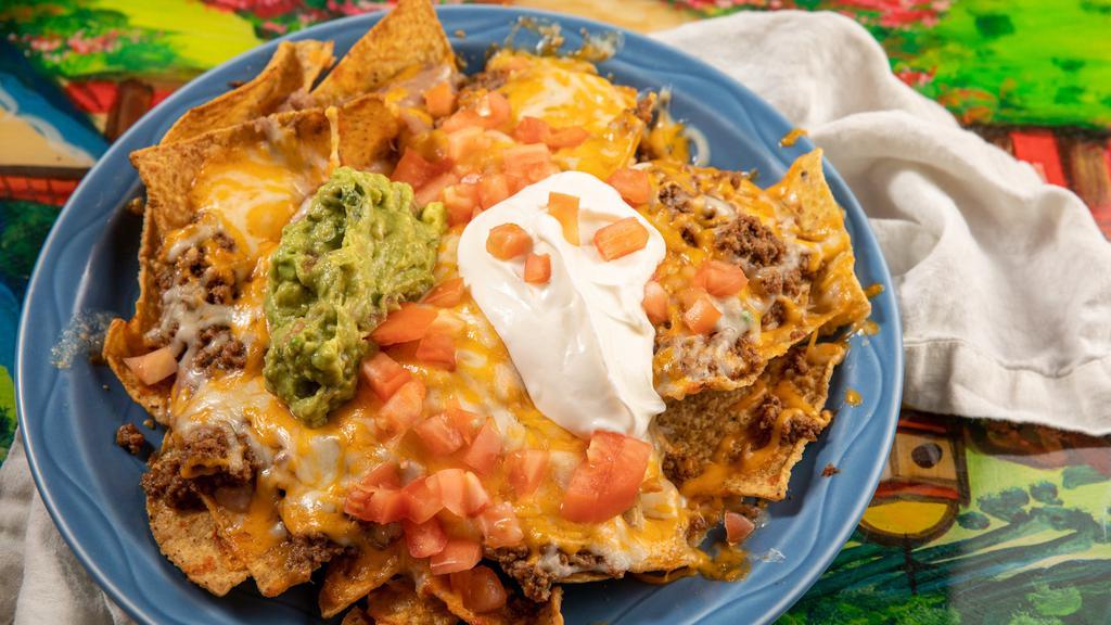 Nachos Supremos Gf · A bed of chips With lettuce, tomato, beans, sour cream, and guacamole.