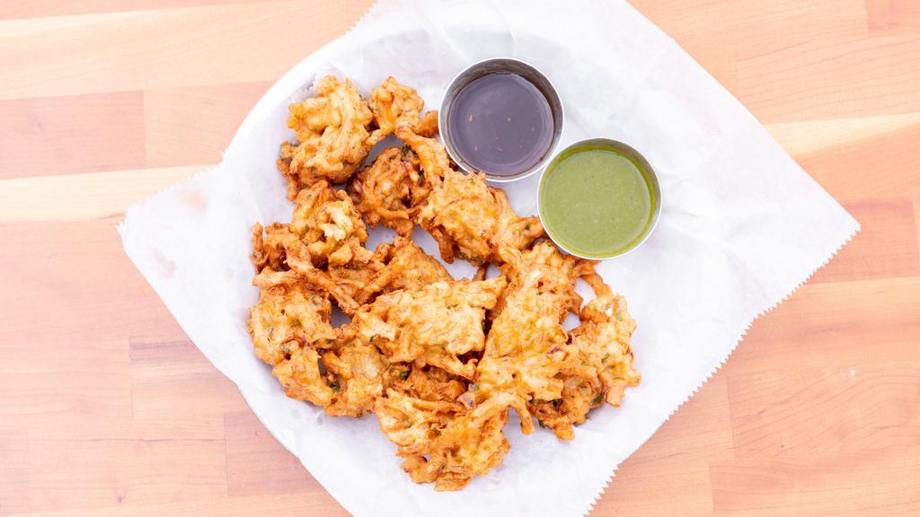 Pakoras · Vegan. Sliced onions, green chilies and cilantro mixed in a batter and fried to crispy puffs. All topped with dry masala and includes green chutney and tamarin sauce.