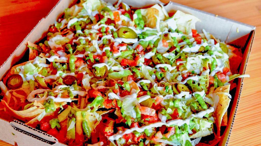Pizza Box Nacho · Stadium-style nachos topped with choice of picadillo beef or chipotle chicken tinga, refried beans, pico de gallo, pickled jalapeños, with a  Mexican crema and avocado crema drizzle.