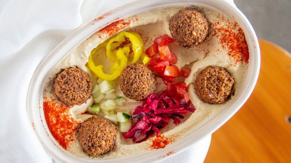 Hummus Bowl · Gluten free and vegan. 
Build your hummus(a blend of pureed chickpeas, tahini, garlic, and extra virgin olive oil.) bowl with your choice of protein, fresh veggies and sauces it up. Comes with 1 pita bread