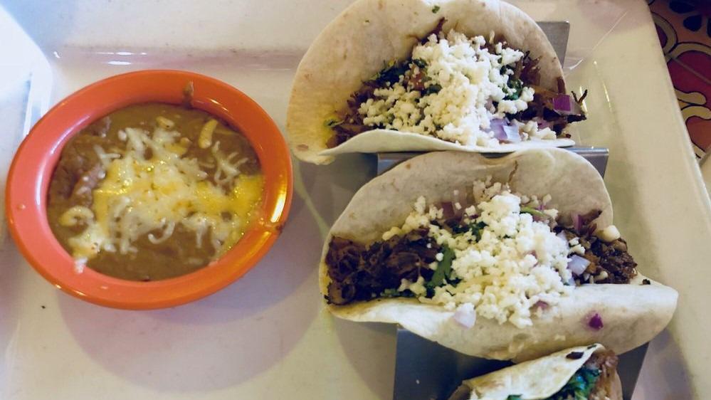 Tacos De Bistek · Thin pieces of steak grilled and served on a flour tortilla. Topped with fresh onions, cilantro, queso fresco and tomatillo drizzle. Served with a side of beans.