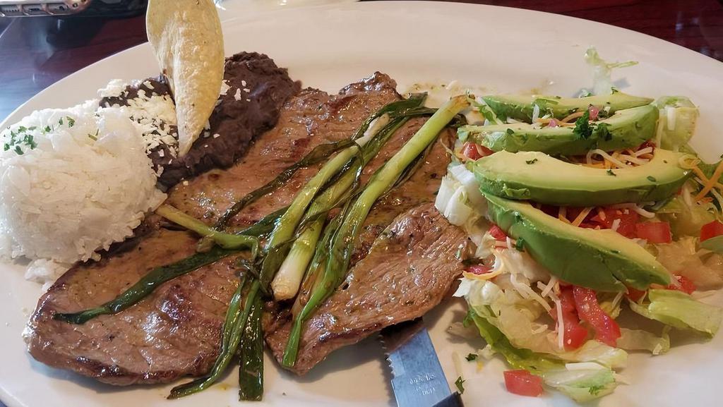 Carne Asada · Grilled beef steak marinated in chimichurri, topped with two green onions, served with rice, refried beans, salad and sliced avocado. With corn tortillas.