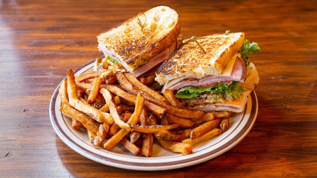 Dagwood Club · Ham, Turkey, Bacon, Swiss, Cheddar, Lettuce, Tomato & House Dressing, stacked up with 3 pieces of toasted Ciabatta, with a side of French Fries.