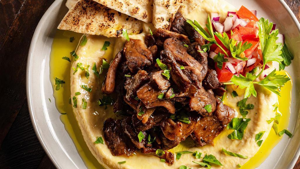 Hummus Beef Shawarma · Seasoned beef  shawarma strips grilled vegetables and onions layered over hummus and served with a side of pita bread.