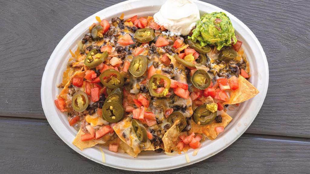 Nachos · fried tortilla chips topped with refried beans, choice of meat, shredded cheese mix melted and topped with tomatoes and jalapeños served with a side of guacamole, sour cream, and salsa