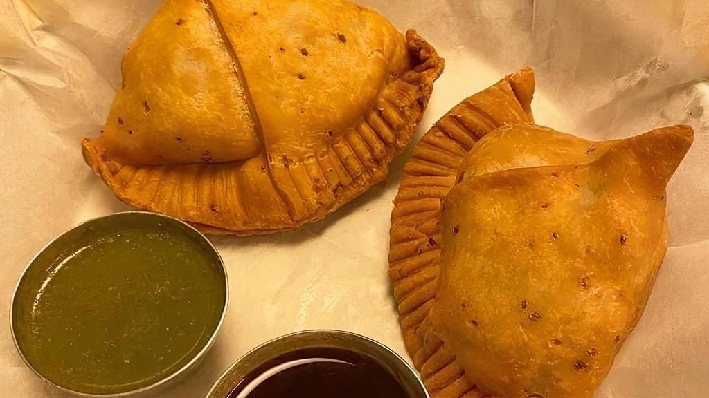Samosa · VEGAN - Seasoned mashed potatoes fried in a pocket with a crispy and crunchy shell. Includes green chutney and tamarind chutney.