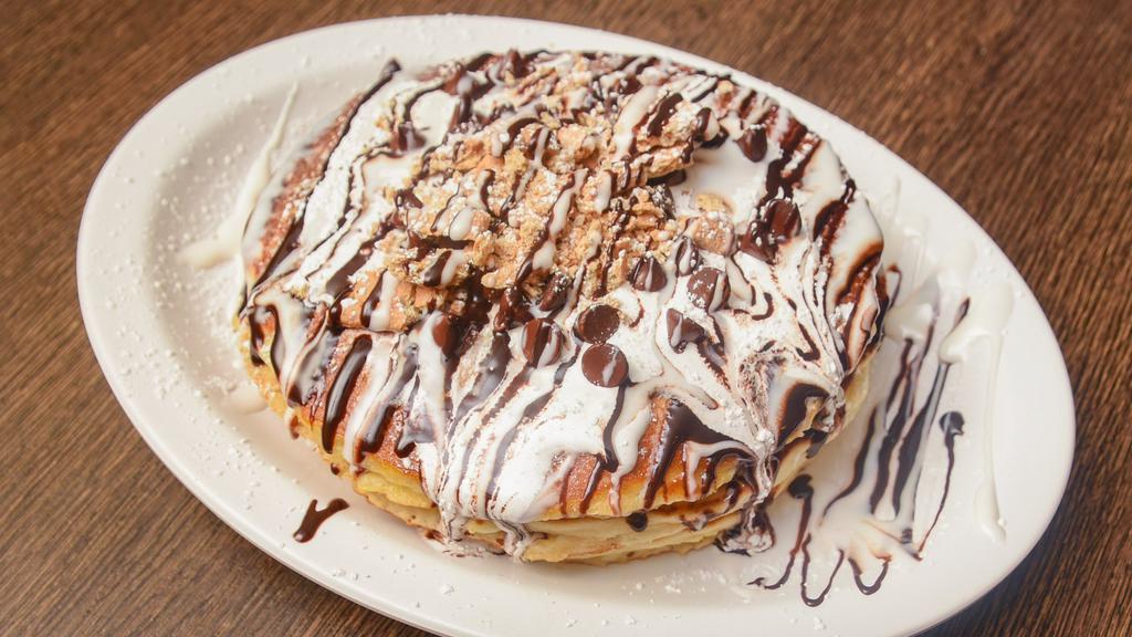 S'Mores Pancakes · Three pieces of pancakes stuffed with chocolate chips, graham cracker, and marshmallow fluff, topped with the same thing and drizzled with chocolate and white chocolate sauce.