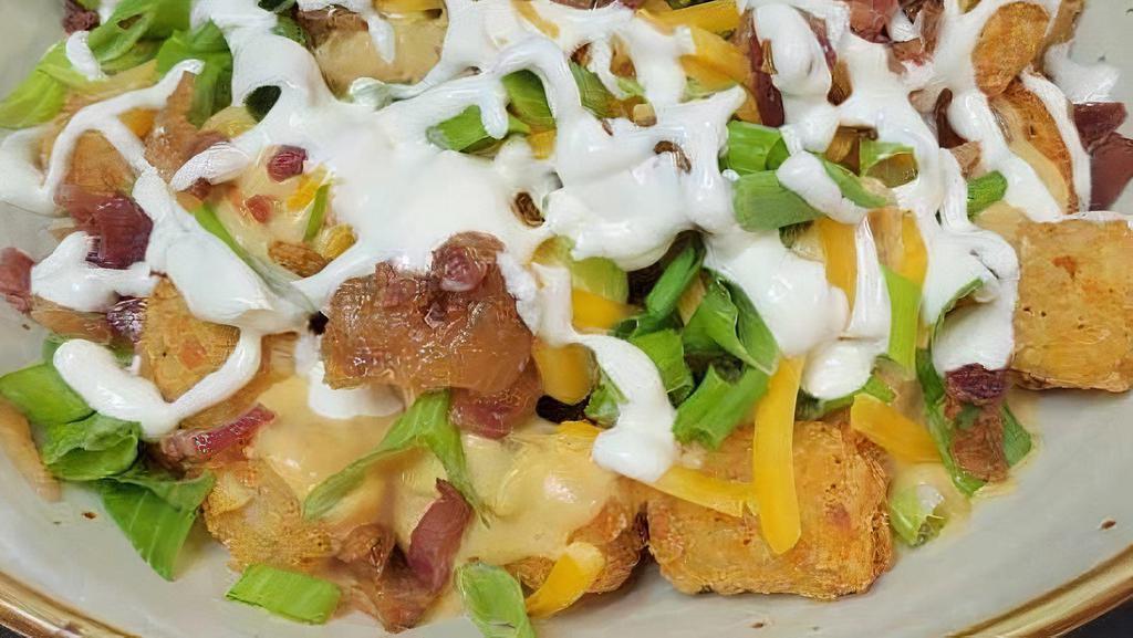 Loaded Tater Tots · Cajun seasoned fries, queso sauce, sour cream drizzle, crisp bacon bits, and onion.