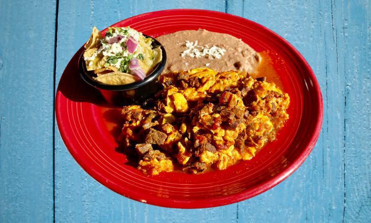 Huevos Aporreados · Scrambled Eggs with Steak & roasted red salsa with a side of Green Chilaquiles and refried beans.