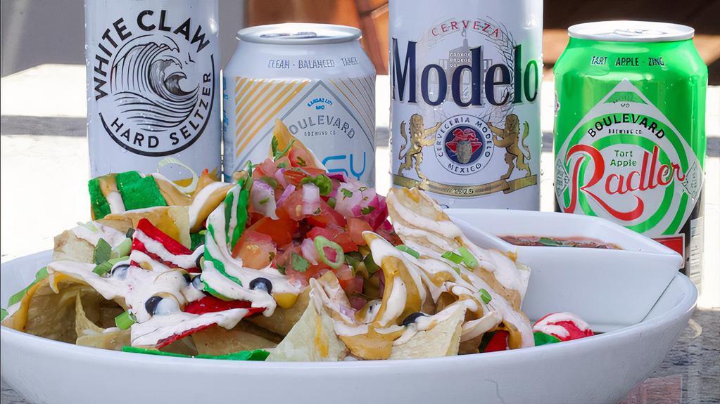 Nachos (V) · A giant pile of locally produced Perez corn tortilla chips topped with mixed cheeses, cheese fondue, vegetarian black beans, Pico de Gallo, and lime crema. Topped with green onions and served with house-made charred tomato salsa.. Indulge by adding spicy marinated Tinga Chicken +$3