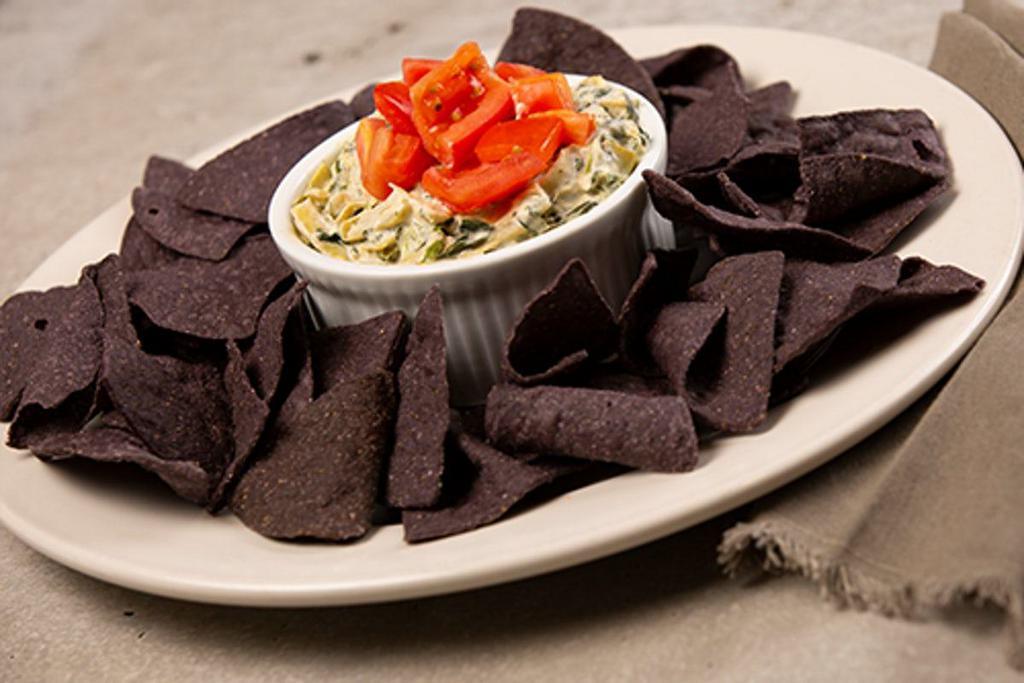 Spinach And Artichoke Dip · creamy dip with artichokes, spinach and diced tomatoes served warm with blue corn tortilla chips