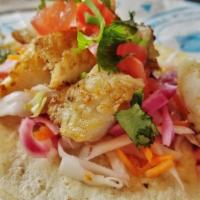 Curtido Fish Taco · Seared pollock, curtido slaw, tomato, and cilantro on a corn tortilla with a lime wedge.
