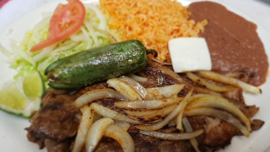 Carne Asada · Bistec asado con cebollas, arroz, frijoles, ensalada y tortillas / fried steak with onions served with a side of rice, beans, salad, and tortillas.