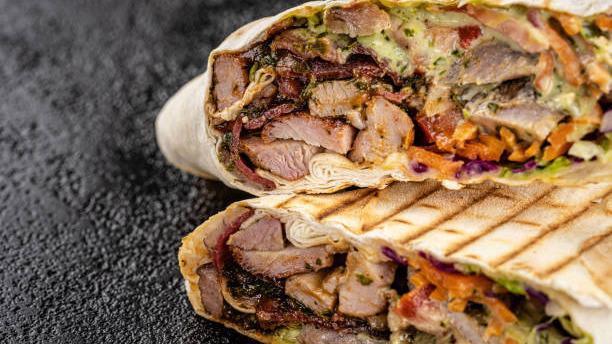Beef Shawarma · Thinly sliced lean inside round steak, marinated over-night,  cooked on a vertical rotisserie , then thinly shaved off onto a bed of rice, and topped with tomatoes, onions and tahini sauce.