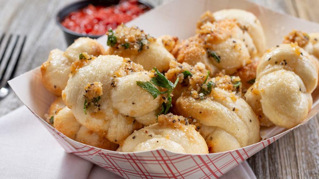 Garlic Knots · Fresh baked garlic knots brushed with olive oil and rolled in chopped garlic, oregano, and parsley, and parmesan cheese with a side of marinara sauce.